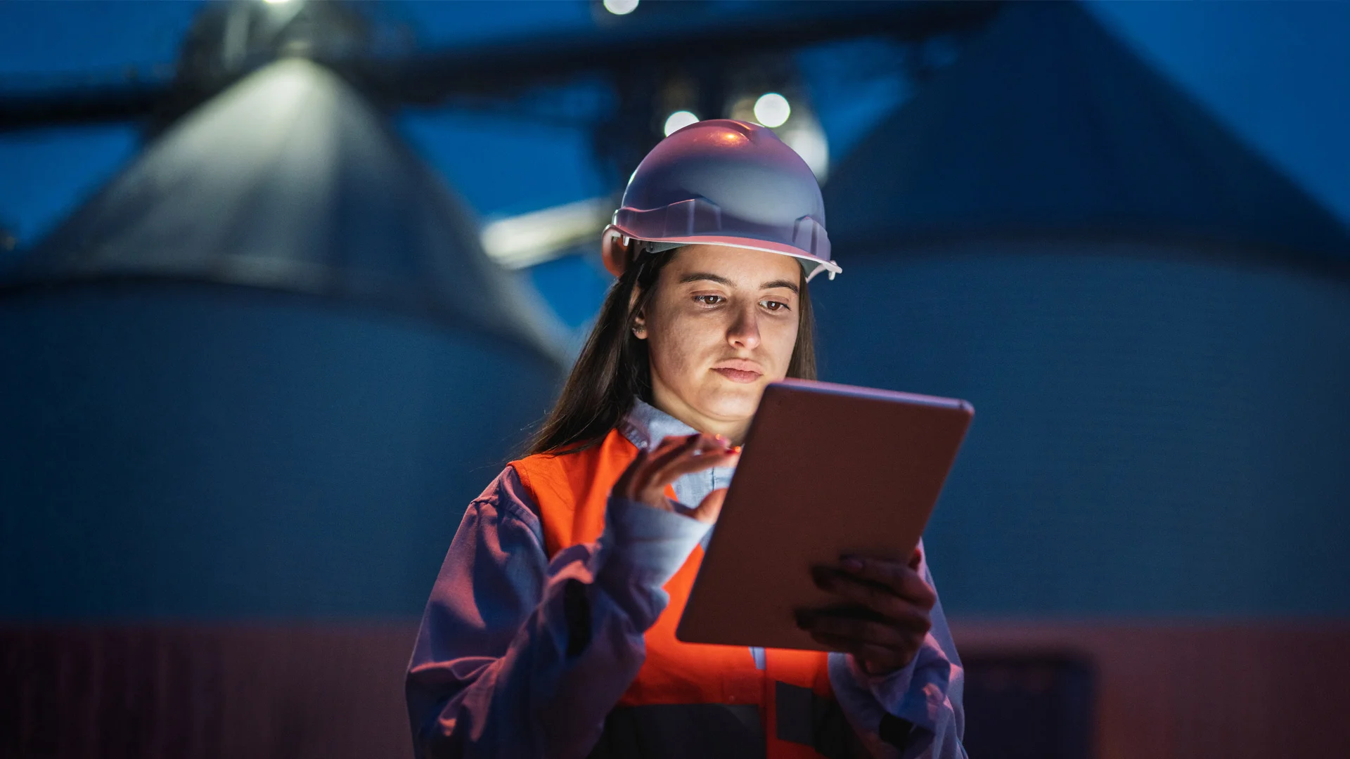 Woman in high vis and hard hat looking at tablet in the dark