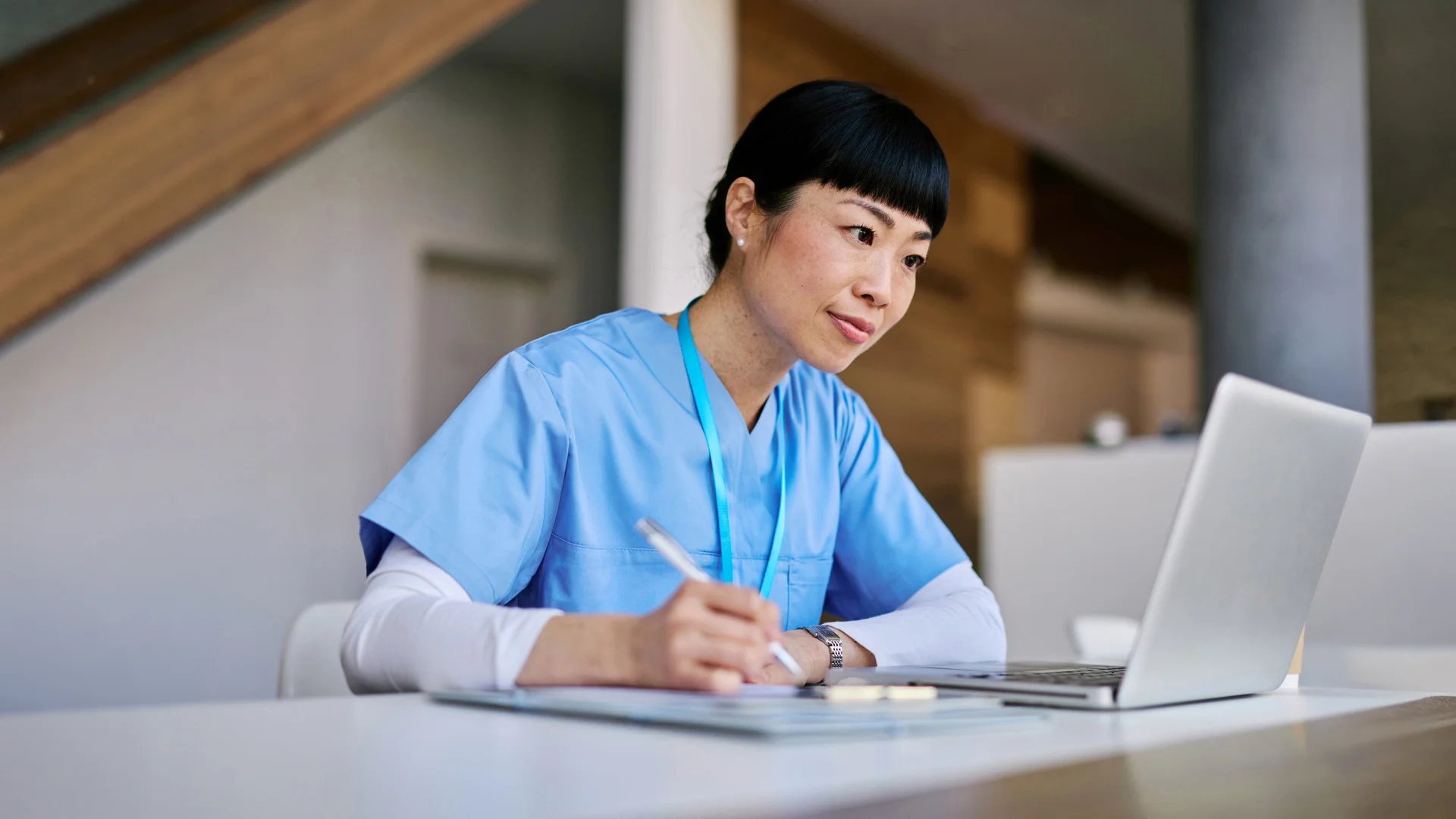 Woman in scrubs making notes and looking at a laptop