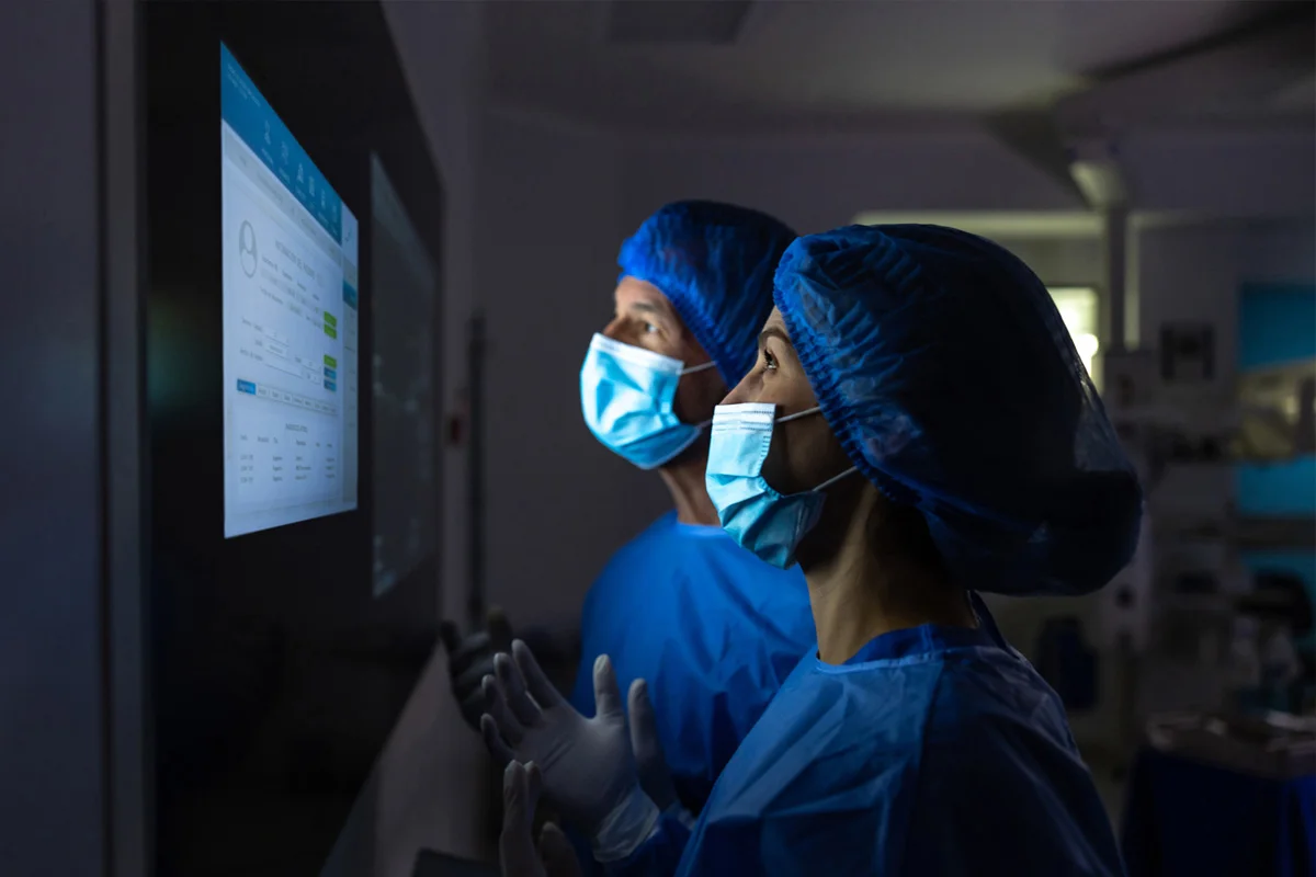 Two surgeons in masks and scrubs looking at screen